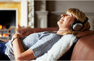 Woman relaxing on a couch with eyes closed listening to headphones while she receives a remote LifeSpark session.
